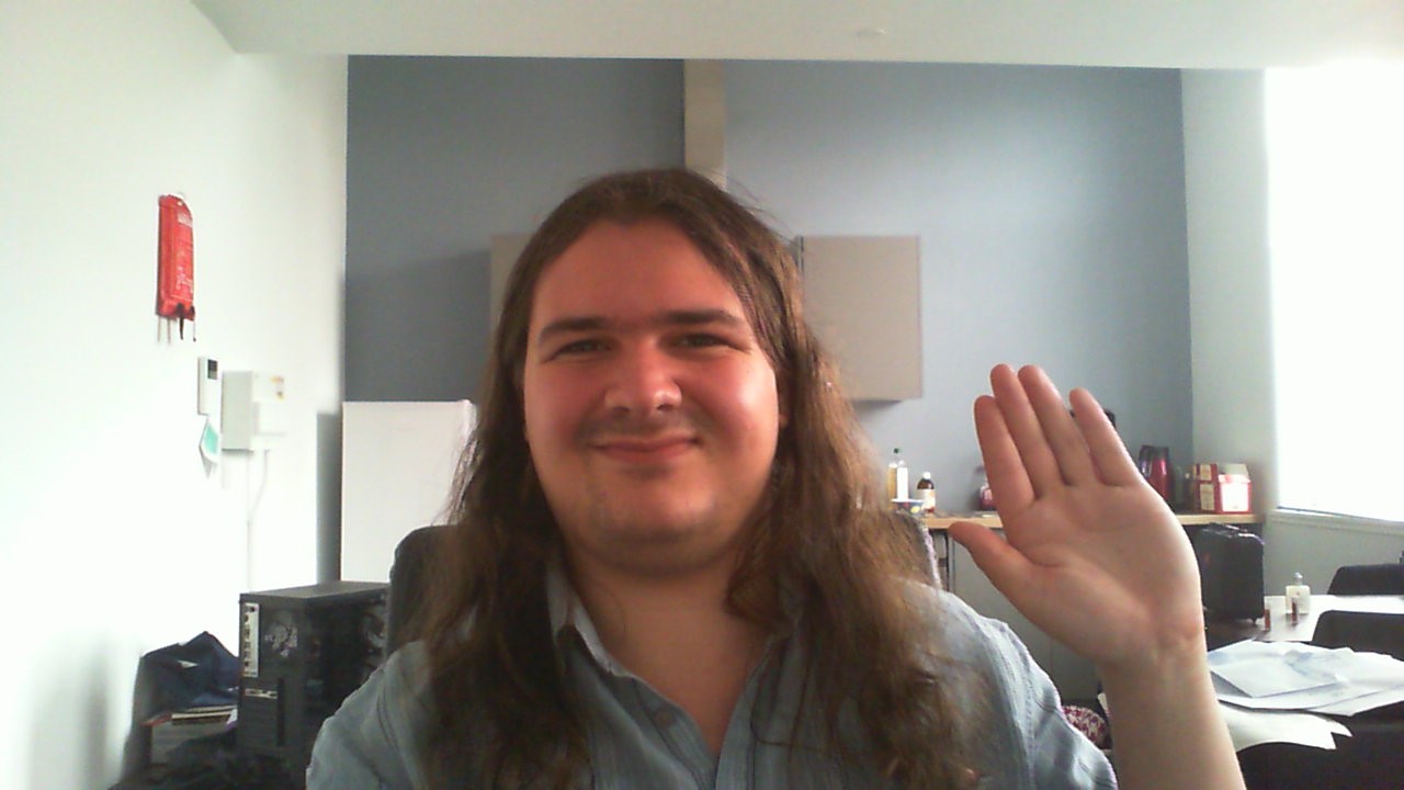 A picture of me, Dagmar, sat at my desk & waving at the camera.